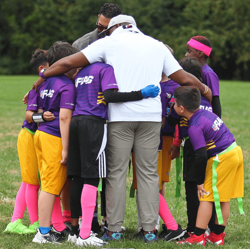 A coach huddles with young players in purple jerseys