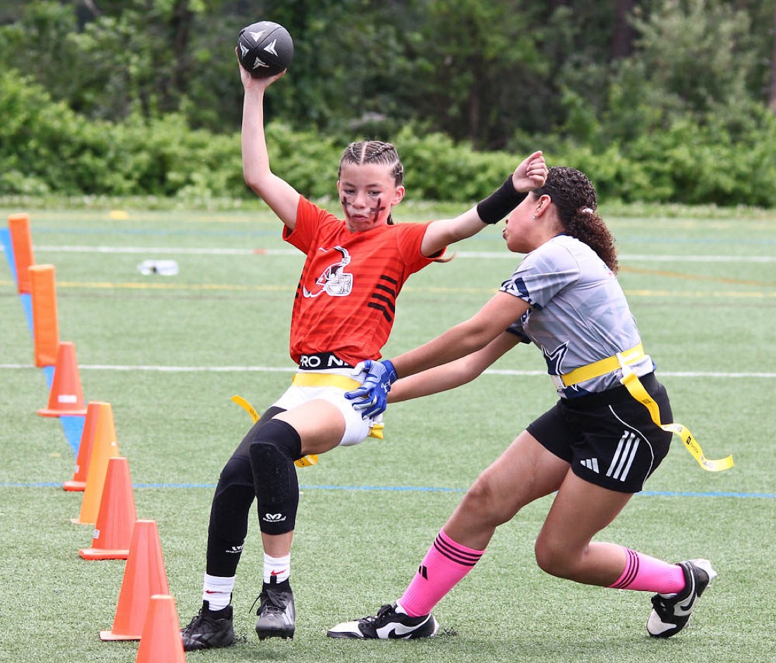 A quarterback throws past a line of cones as a defender reaches