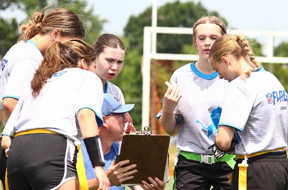 A coach with a clipboard talks with players