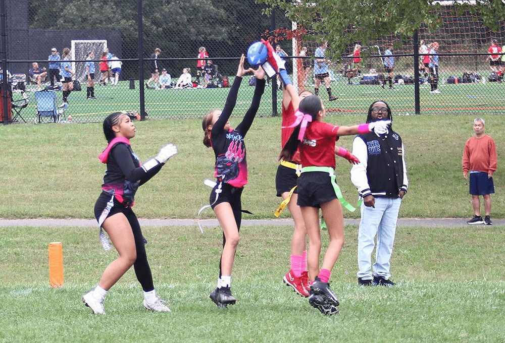 All-Girls players leap for a pass with families watching